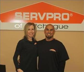man and woman posing in black s shirts in front of logo sign