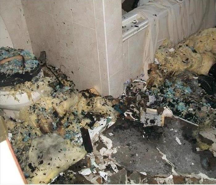 Heavy fire damage debris in a bathroom covering the tub and toilet with soot, drywall, and insulation